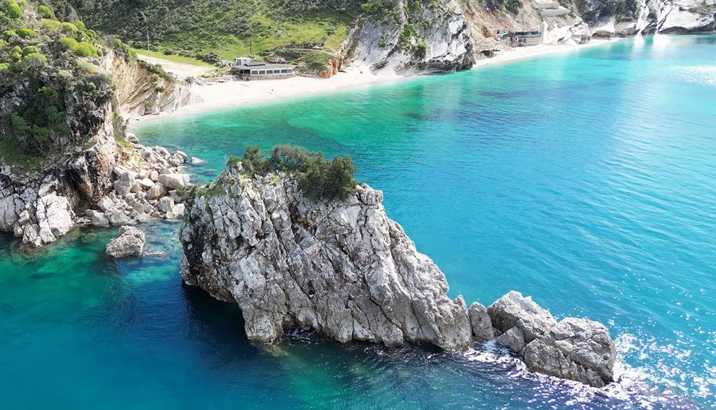 Sunlit waves reflecting off the clear blue waters of Mirror Beach, surrounded by rocky cliffs.